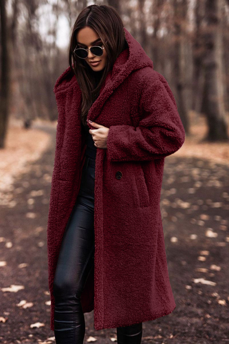 Femme portant un manteau en fausse fourrure bordeaux, lunettes de soleil noires, marchant dans un parc automnal. Mode hiver, style élégant.