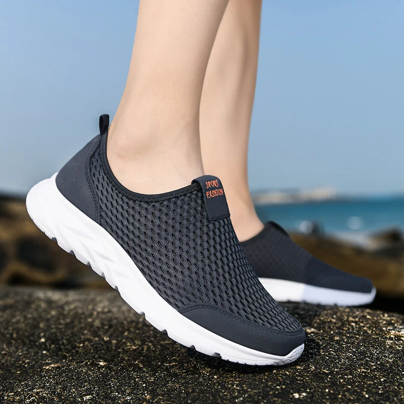 Chaussures de sport légères en maille noire pour homme, semelle blanche, idéales pour la course et le fitness, portées en extérieur sur fond de mer.