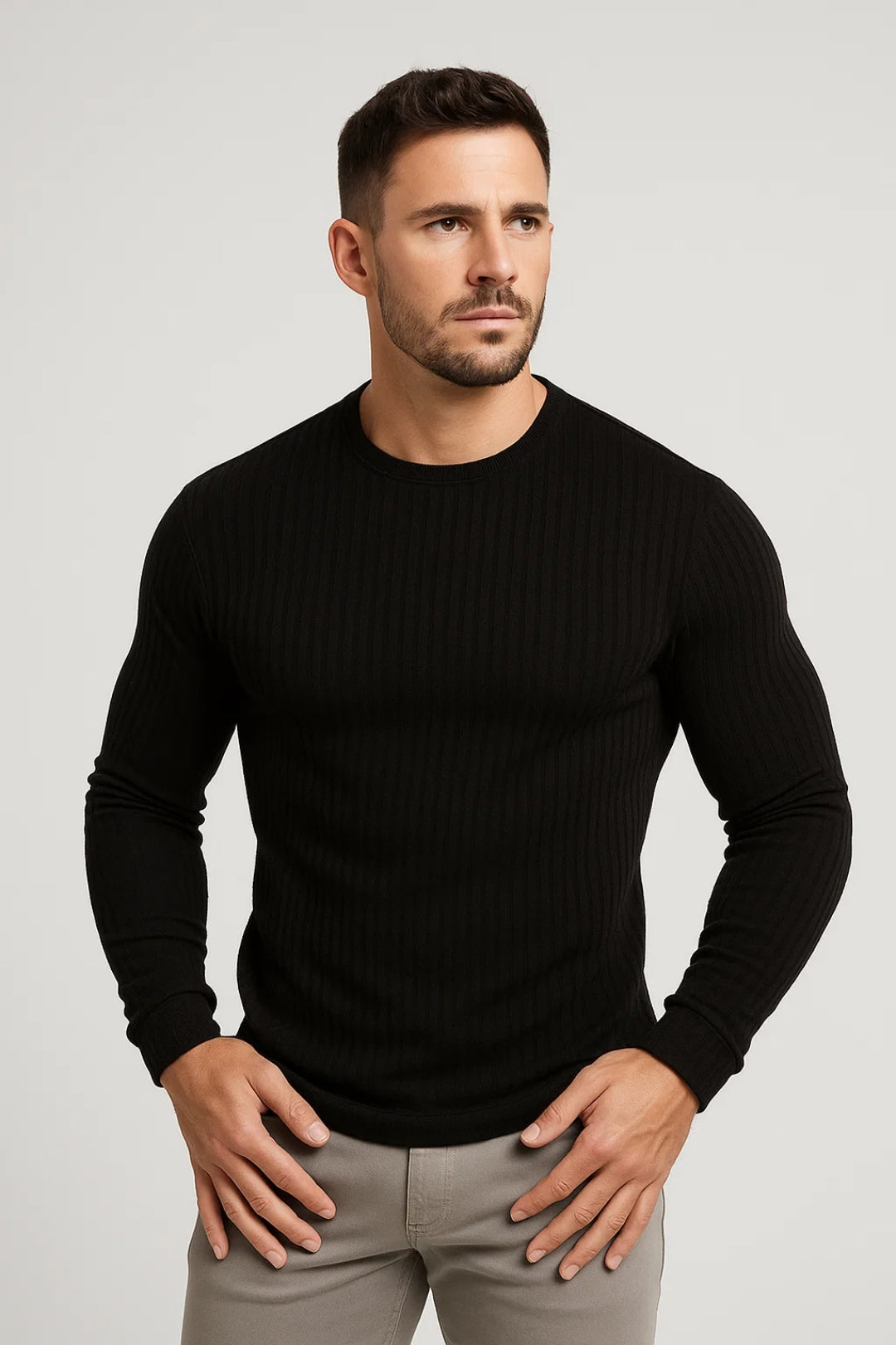 Homme portant un pull noir ajusté, manches longues, col rond, avec un pantalon gris. Mode masculine élégante, style décontracté chic.
