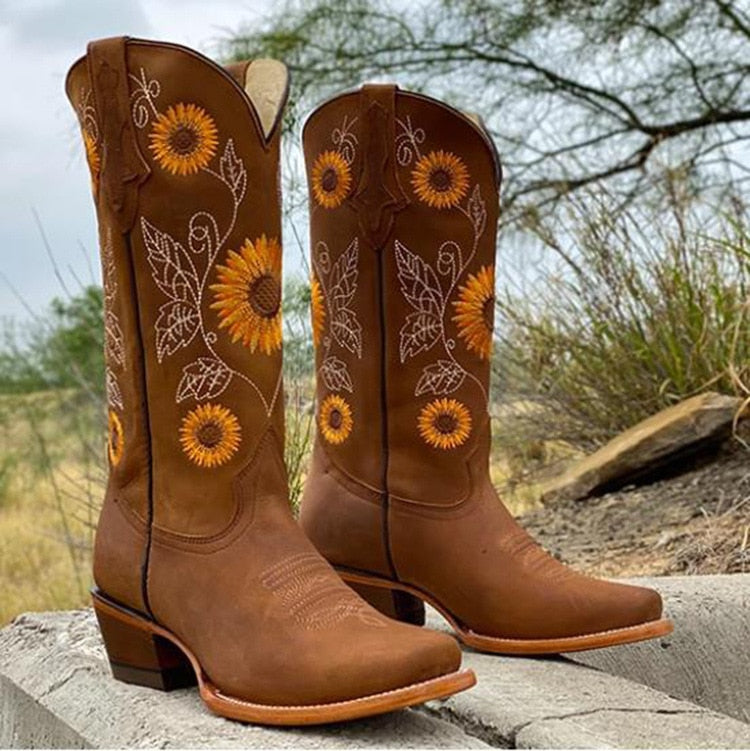 Brune cowboystøvler med solsikke-broderi, placeret udendørs på beton. Stilfulde westernstøvler til kvinder, perfekt til countrymode og festivaler.