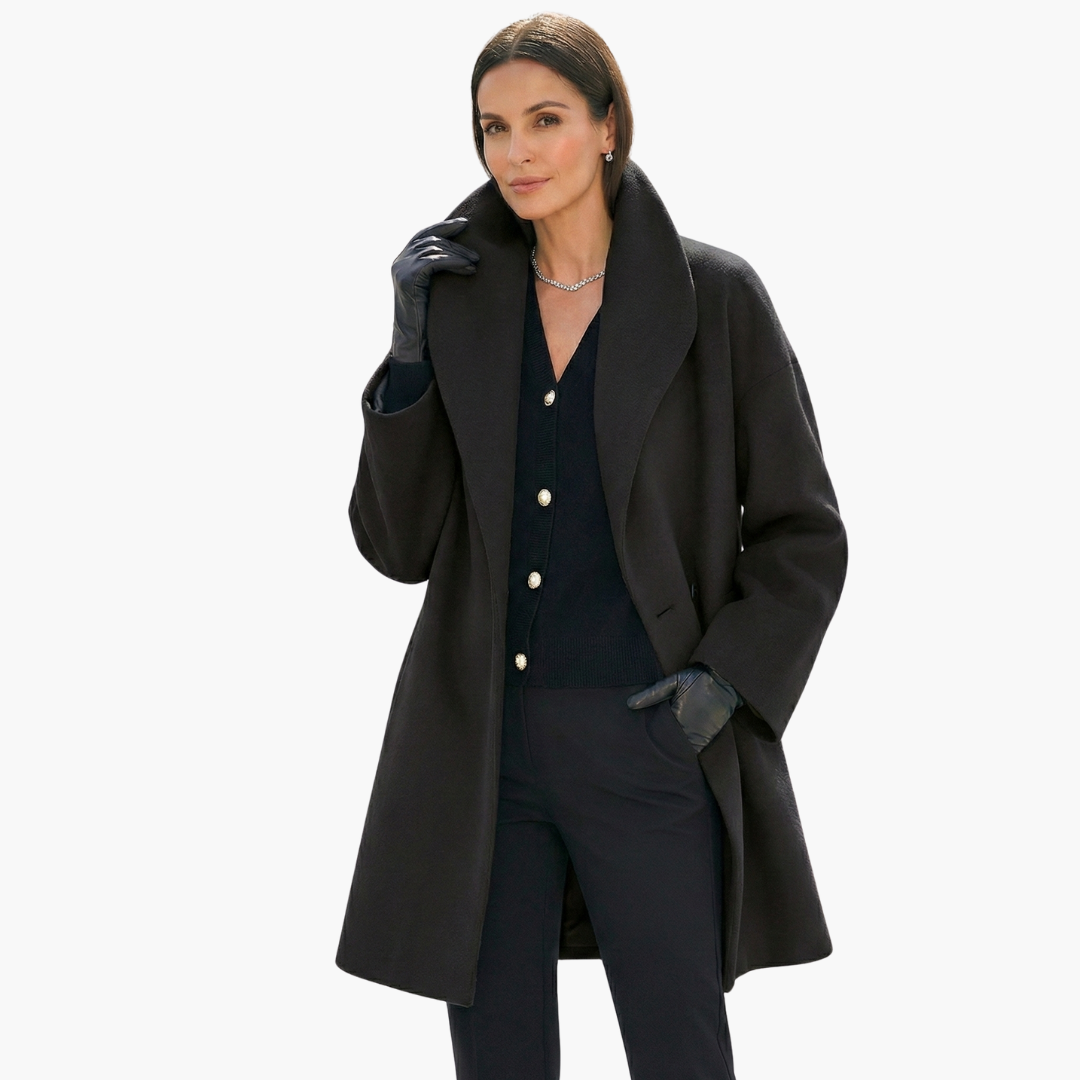 Femme portant un manteau noir élégant, gants en cuir, collier argenté, sur fond blanc. Mode automne-hiver, style chic et sophistiqué.