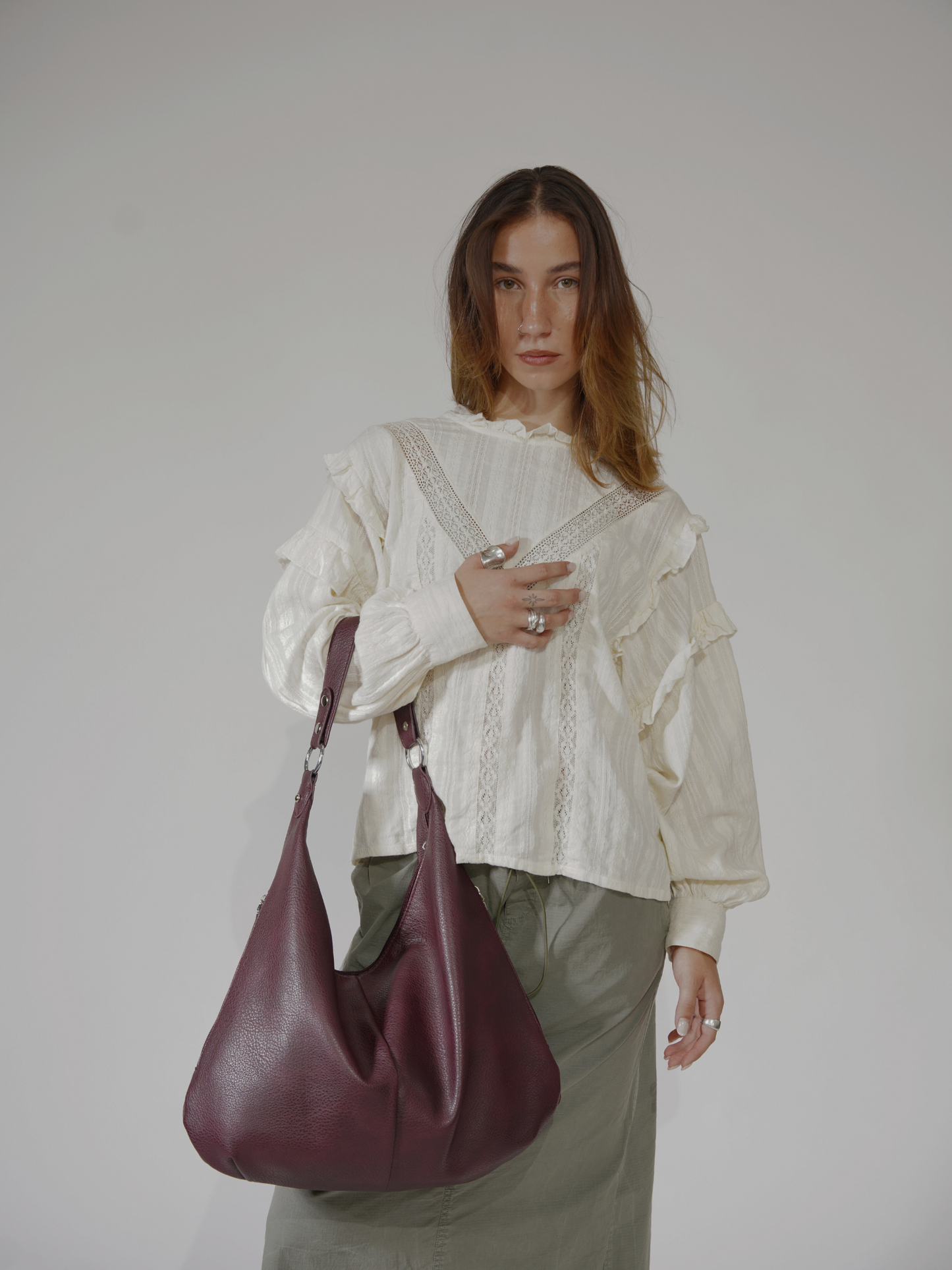 Kvinde i hvid bluse og grøn nederdel bærer en stor, bordeaux skuldertaske. Mode, stilfuldt outfit, moderne accessories.