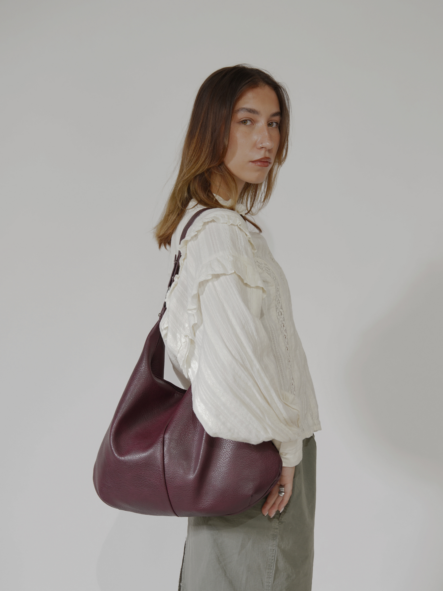Kvinde med hvid bluse og grå nederdel bærer stor bordeaux skuldertaske. Mode, stilfuldt tilbehør, moderne kvindemode, elegant taske.