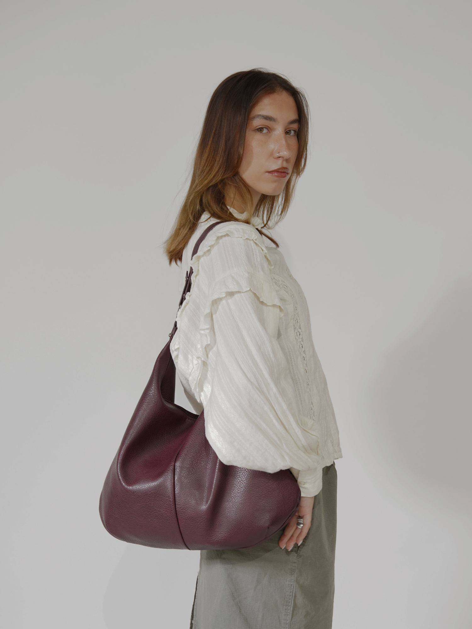 Kvinde med hvid bluse og grå nederdel bærer stor bordeaux skuldertaske. Mode, stilfuldt tilbehør, moderne kvindemode, elegant taske.