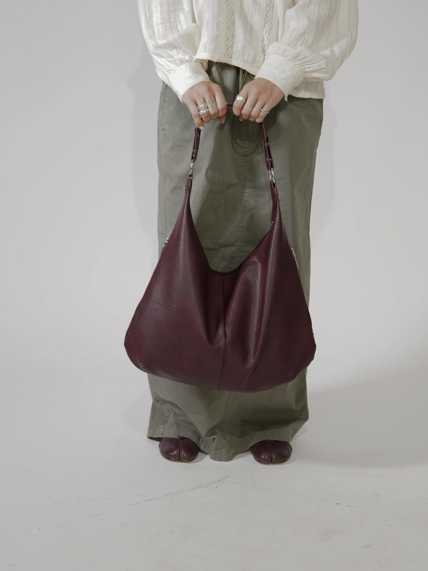 Person i hvid bluse og grønne bukser holder en stor, bordeaux lædertaske. Mode, accessories, stilfuld taske, moderne design.