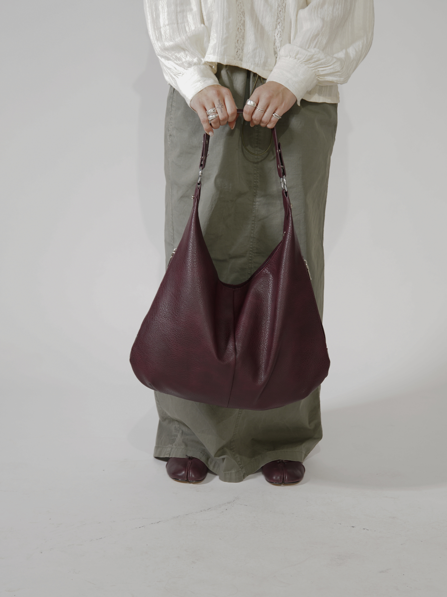 Person i hvid bluse og grønne bukser holder en stor, bordeaux lædertaske. Mode, accessories, stilfuld taske, moderne design.