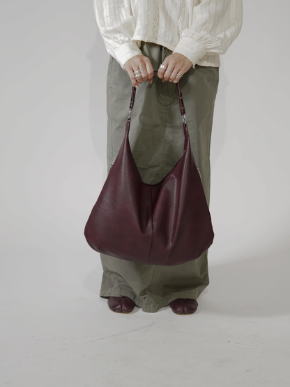 Person i hvid bluse og grønne bukser holder en stor, bordeaux lædertaske. Mode, accessories, stilfuld taske, moderne design.