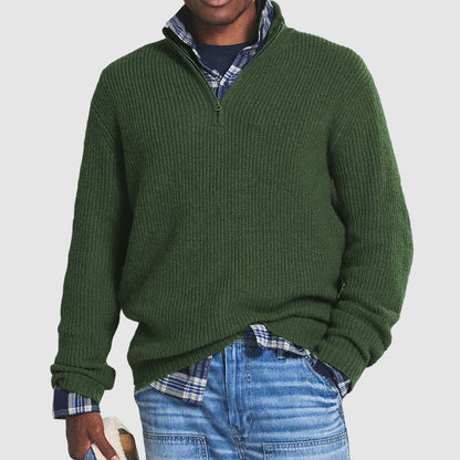 Homme portant un pull vert à col zippé sur une chemise à carreaux bleue, avec un jean décontracté. Mode masculine automne-hiver, style décontracté.