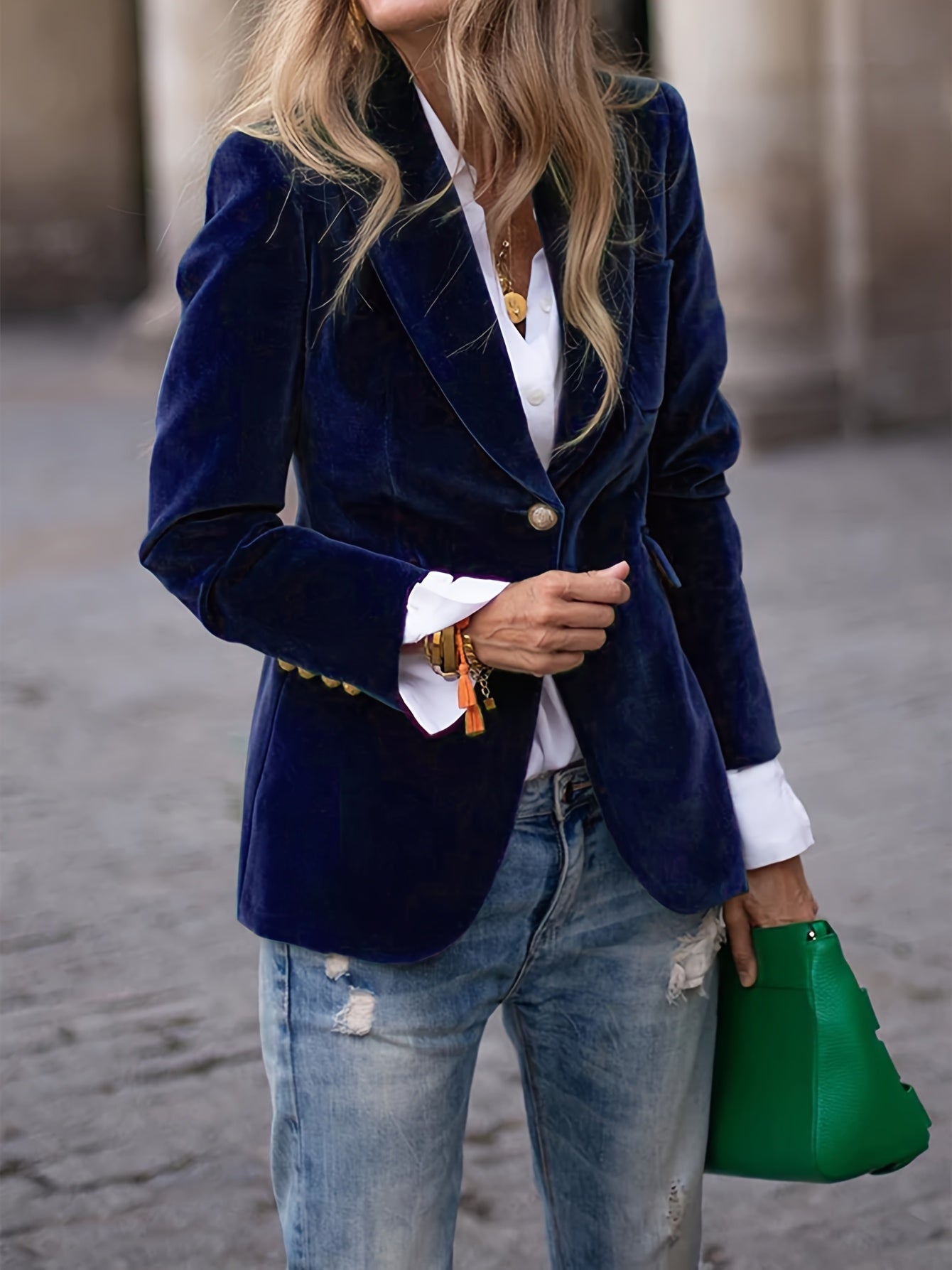 Femme en blazer bleu marine en velours, chemise blanche, jeans déchirés, tenant un sac vert. Mode élégante, tenue décontractée chic.