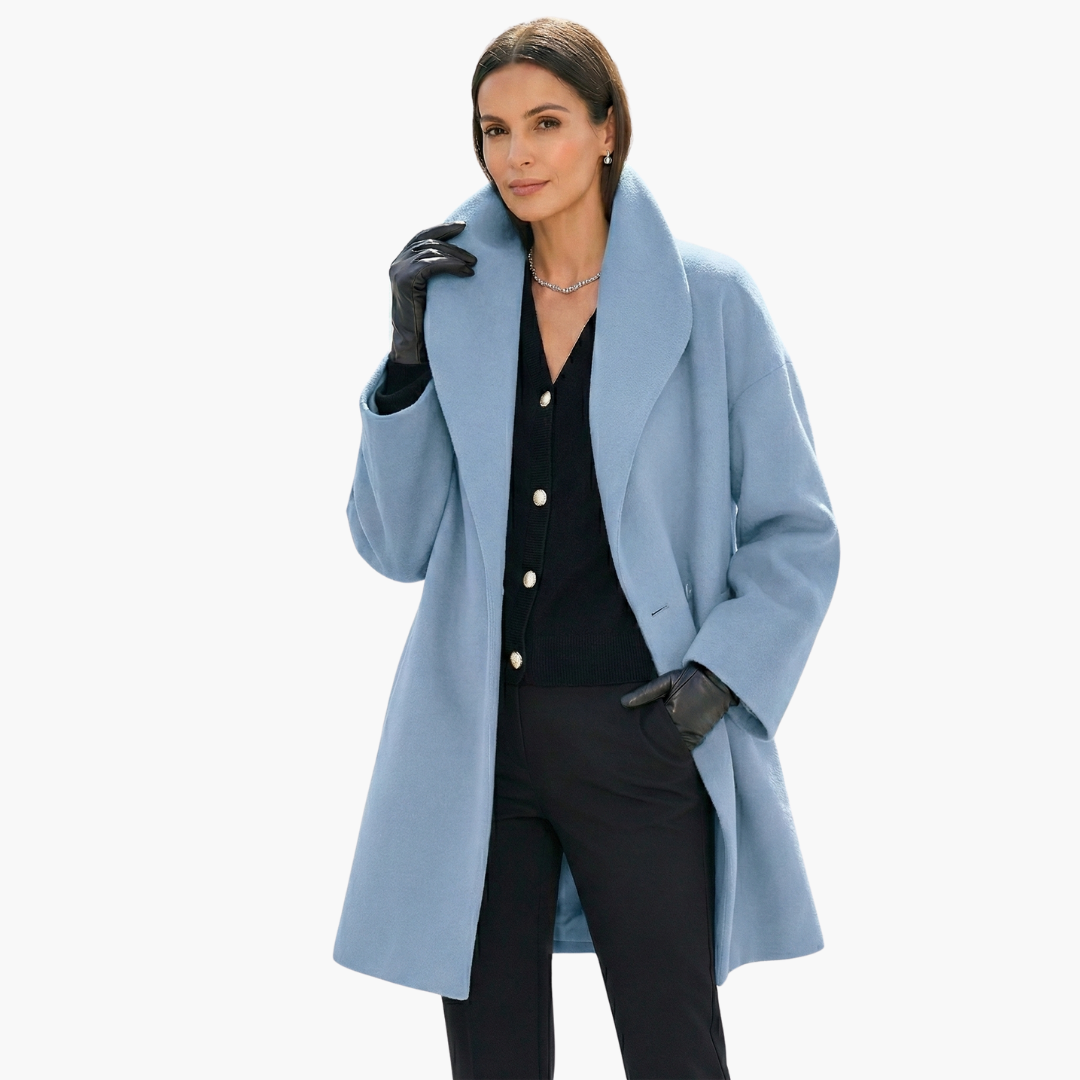 Femme portant un manteau bleu élégant, gants noirs et chemise noire, posant avec assurance. Mode automne-hiver, style chic et moderne.