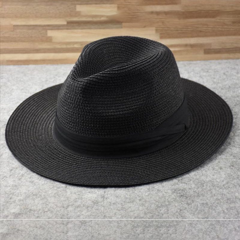 Chapeau Fedora noir en paille tressée sur fond gris, élégant et tendance, idéal pour un look chic et décontracté. Accessoire mode intemporel.