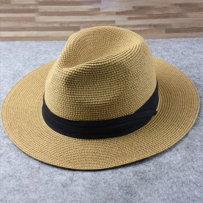 Chapeau fedora en paille beige avec bande noire, posé sur une surface grise. Accessoire de mode élégant pour l'été et protection solaire.