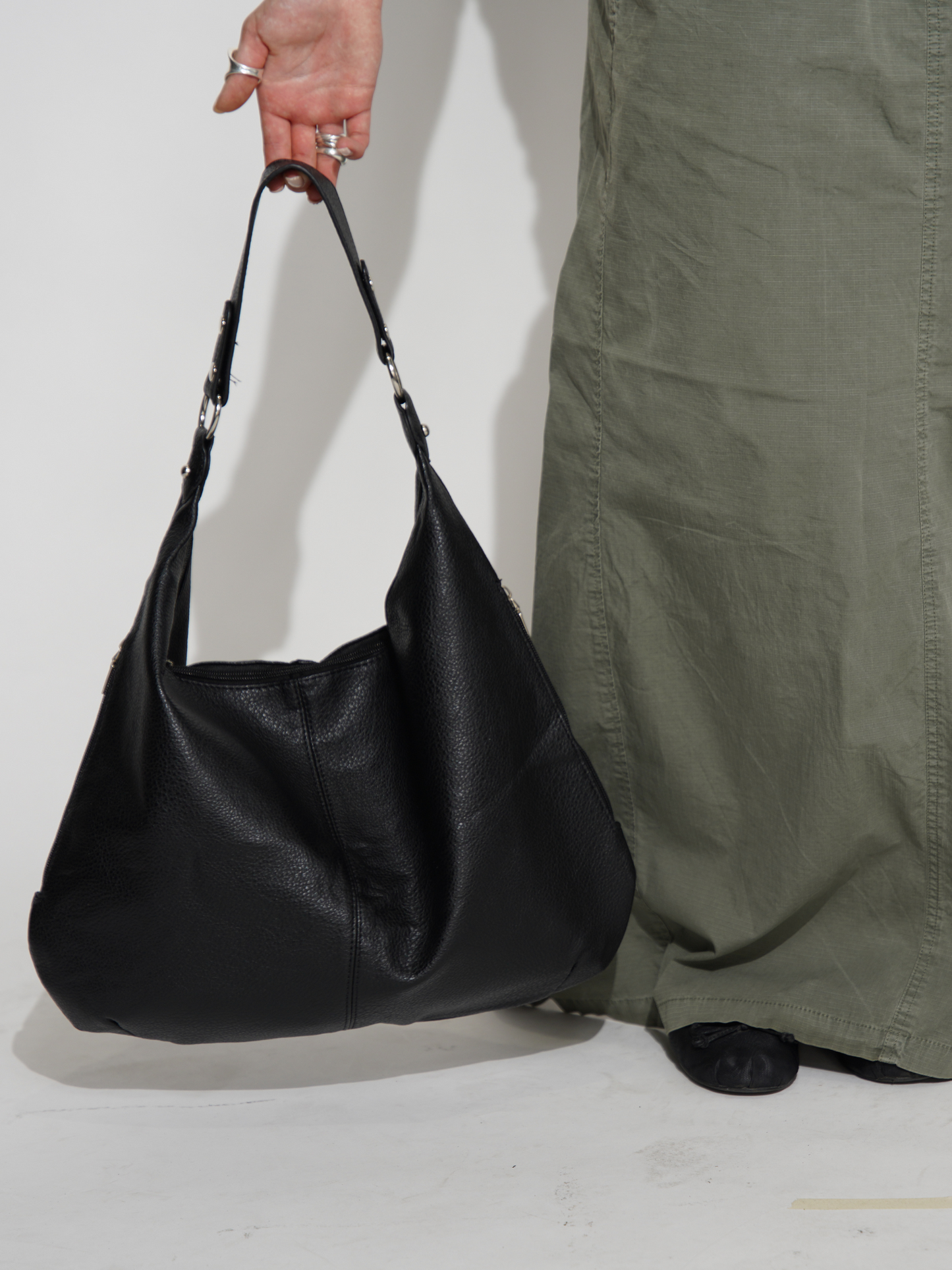 Sort læderhåndtaske bæres af person i grøn nederdel. Stilfuld modeaccessory, perfekt til hverdagsbrug. Trendy og praktisk design.