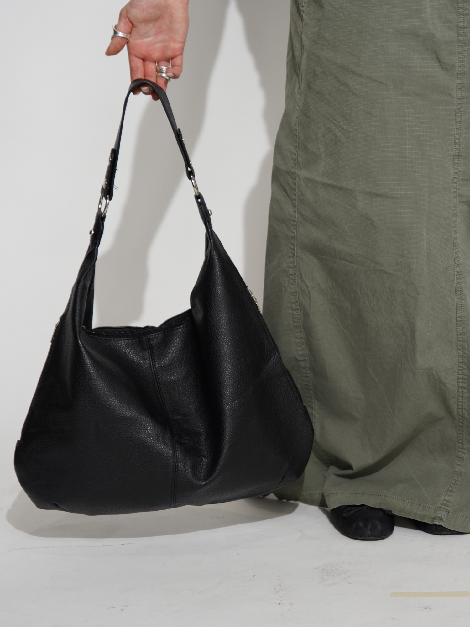 Sort læderhåndtaske bæres af person i grøn nederdel. Stilfuld modeaccessory, perfekt til hverdagsbrug. Trendy og praktisk design.