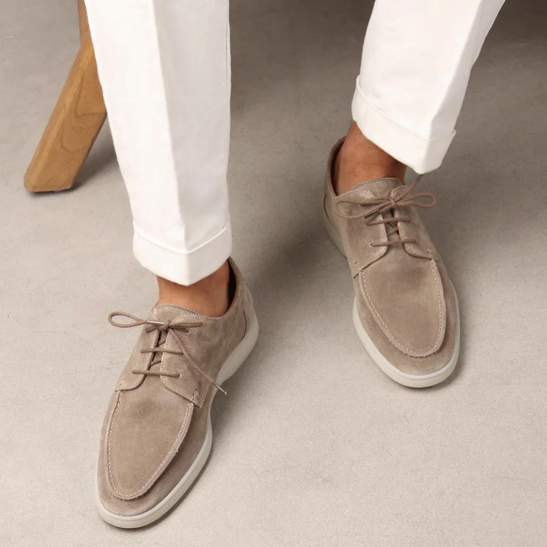 Chaussures derby en daim beige pour homme, élégantes et modernes, portées avec un pantalon blanc. Mode masculine, style décontracté chic.