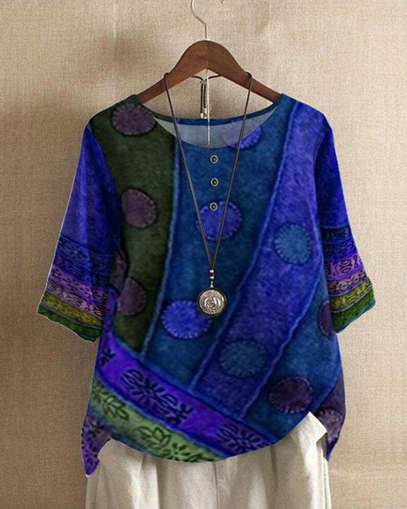 Blouse bohème chic bleue à motifs ethniques, manches trois-quarts, col rond avec boutons, suspendue sur un cintre en bois.