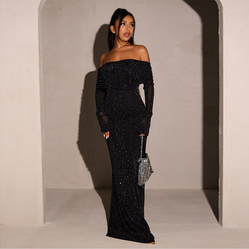 Robe longue noire à paillettes, épaules dénudées, manches longues, portée par une femme avec un sac à main argenté scintillant.