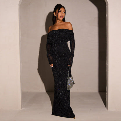 Robe longue noire à paillettes, épaules dénudées, manches longues, portée par une femme avec un sac à main argenté scintillant.