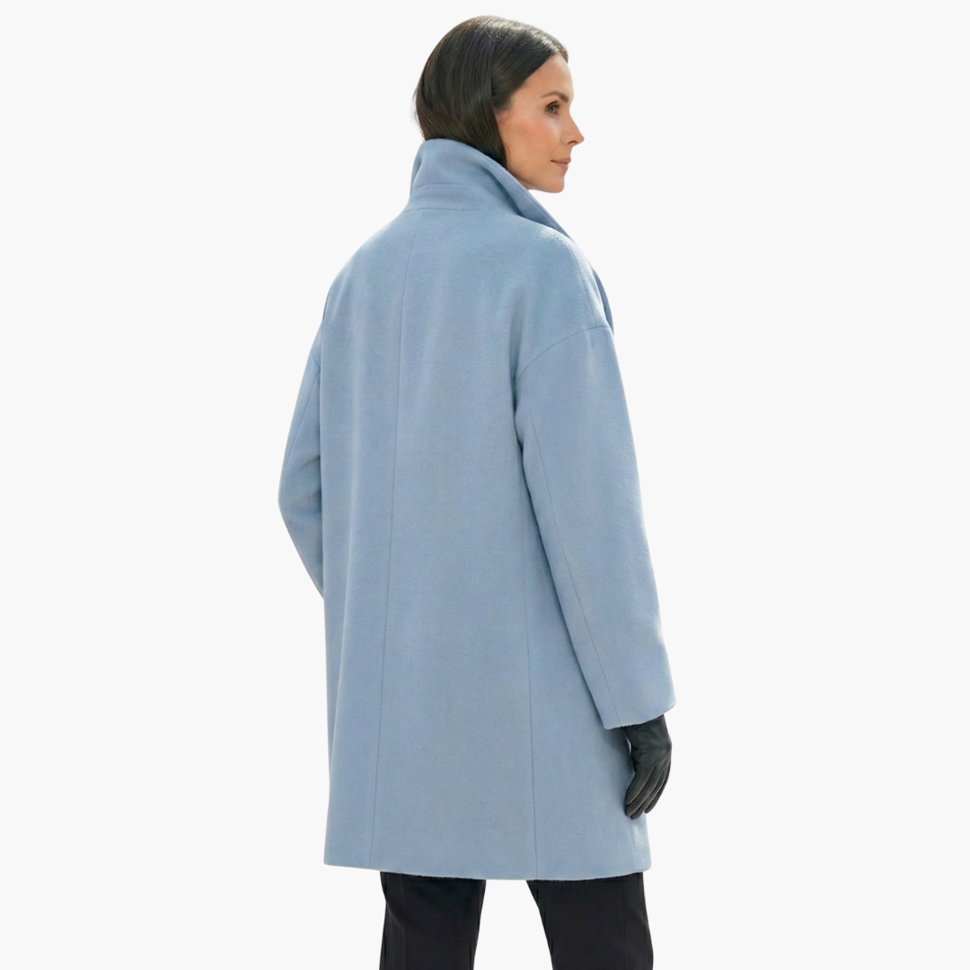 Manteau bleu ciel femme, coupe ample, col montant, manches longues, porté avec des gants noirs. Mode hiver élégante et moderne.