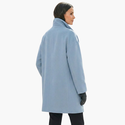 Manteau bleu ciel femme, coupe ample, col montant, manches longues, porté avec des gants noirs. Mode hiver élégante et moderne.