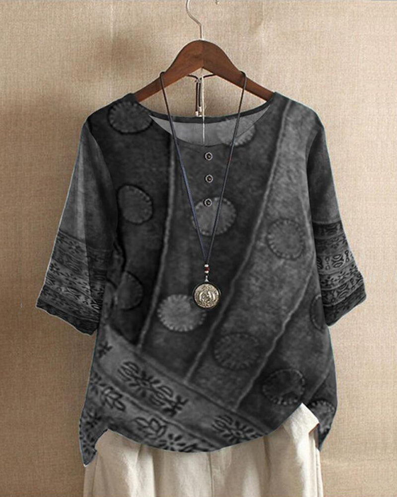Blouse en lin gris à motifs ethniques, manches trois-quarts, col rond avec boutons, suspendue sur un cintre en bois, fond beige.