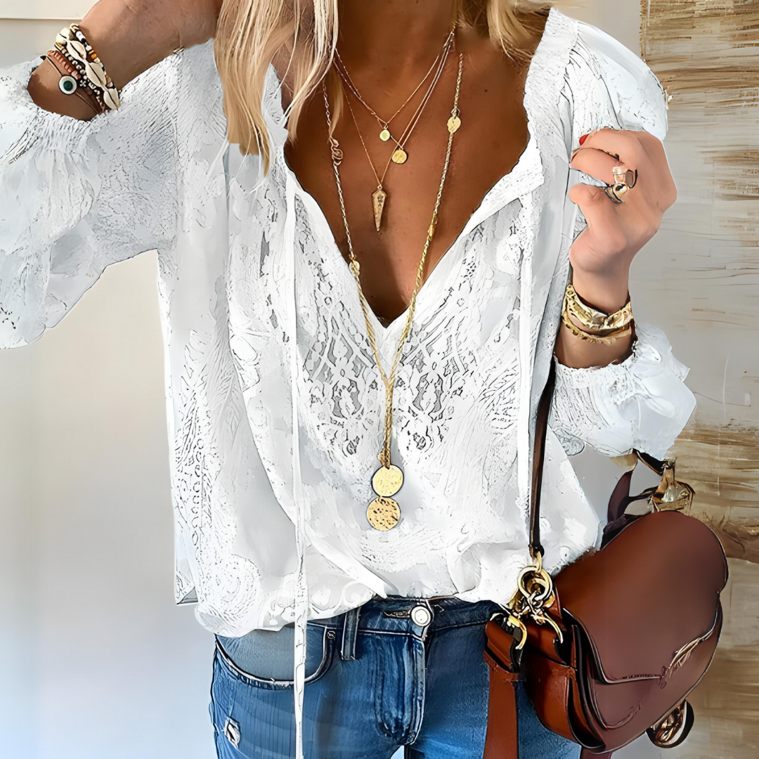 Femme portant un chemisier blanc en dentelle, colliers dorés superposés, jean bleu, sac à main marron. Mode féminine élégante et tendance.