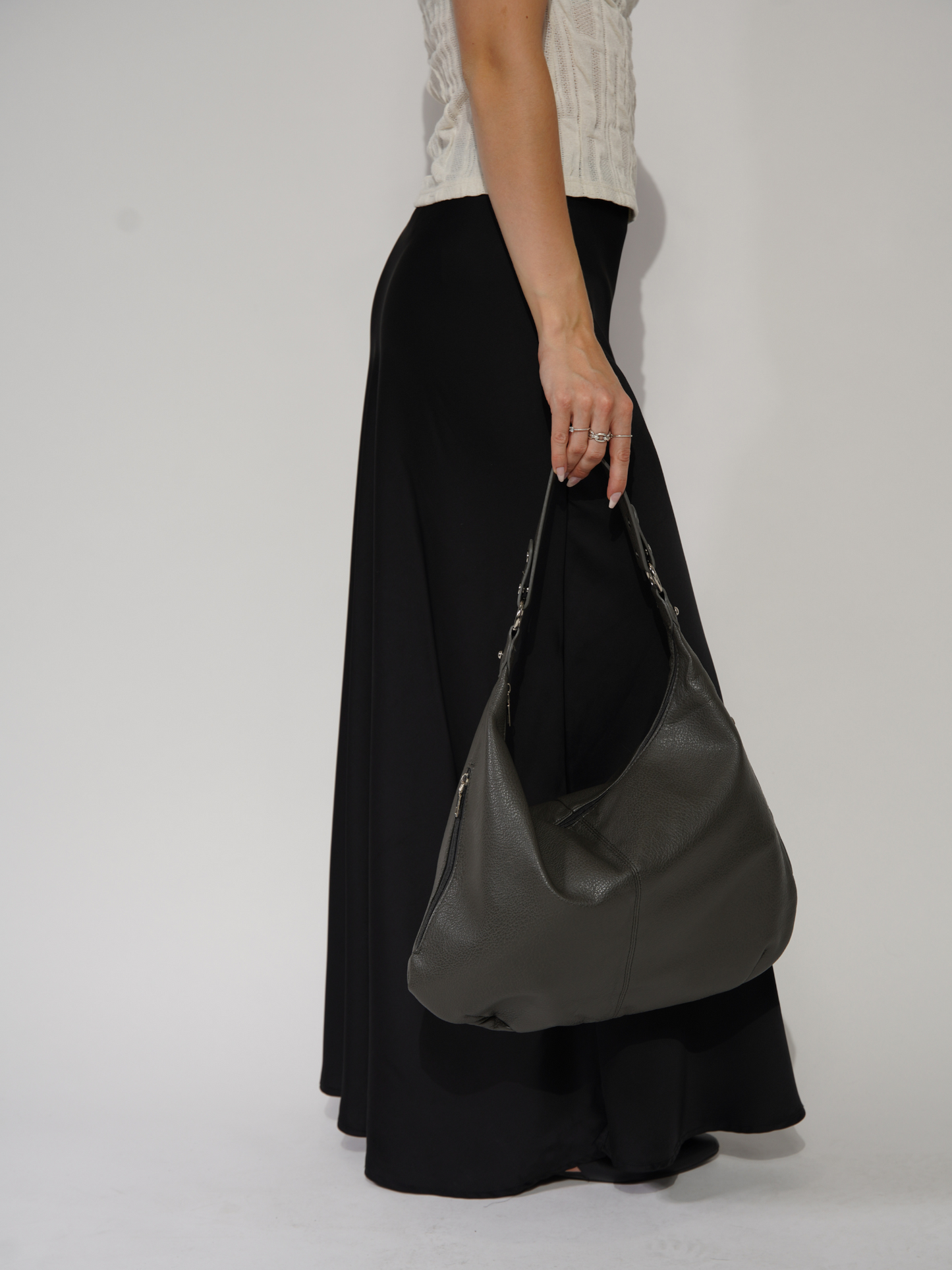 Kvinde i sort nederdel og hvid top holder en grå lædertaske. Mode, stilfuldt tilbehør, moderne kvindemode, elegant håndtaske.