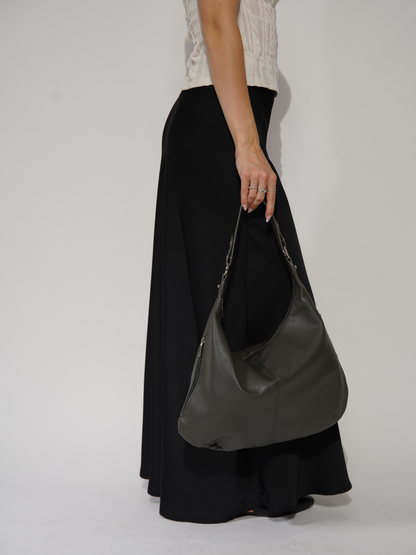 Kvinde i sort nederdel og hvid top holder en grå lædertaske. Mode, stilfuldt tilbehør, moderne kvindemode, elegant håndtaske.