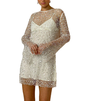 Robe courte transparente à paillettes argentées, manches longues, portée par une femme. Mode élégante, tenue de soirée glamour.