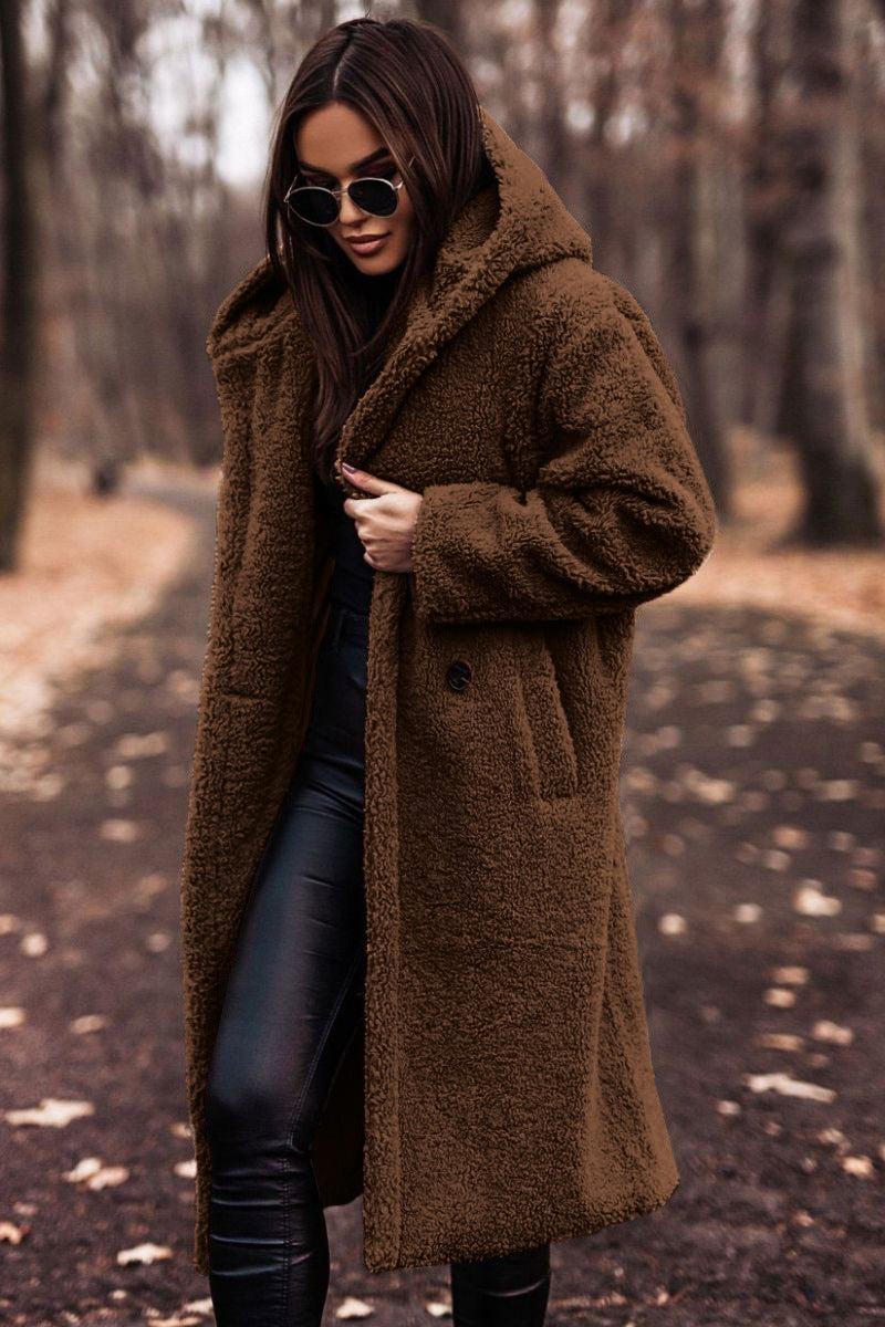 Femme portant un manteau en fausse fourrure marron, lunettes de soleil noires, dans un parc automnal. Mode hiver, style chic, tendance.