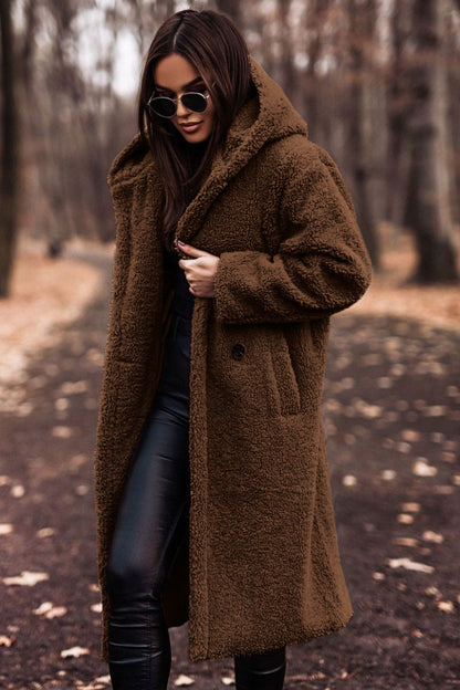 Femme portant un manteau en fausse fourrure marron, lunettes de soleil noires, dans un parc automnal. Mode hiver, style chic, tendance.