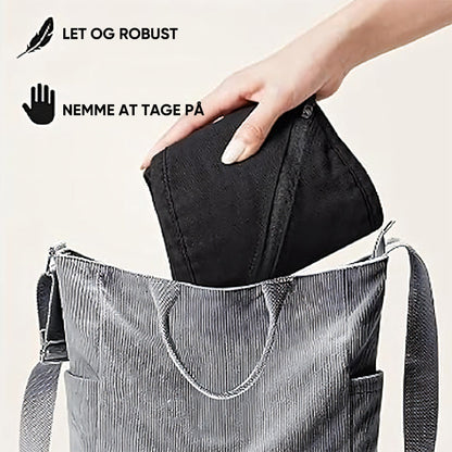 Sac à main gris avec une main insérant une pochette noire. Texte en danois: "Let og robust, nemme at tage på". Accessoire mode pratique et élégant.