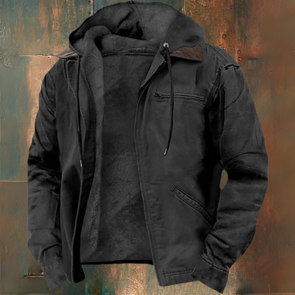 Veste noire à capuche en tissu épais, avec doublure en fourrure synthétique, poches zippées, sur fond texturé. Mode hiver, vêtement chaud.