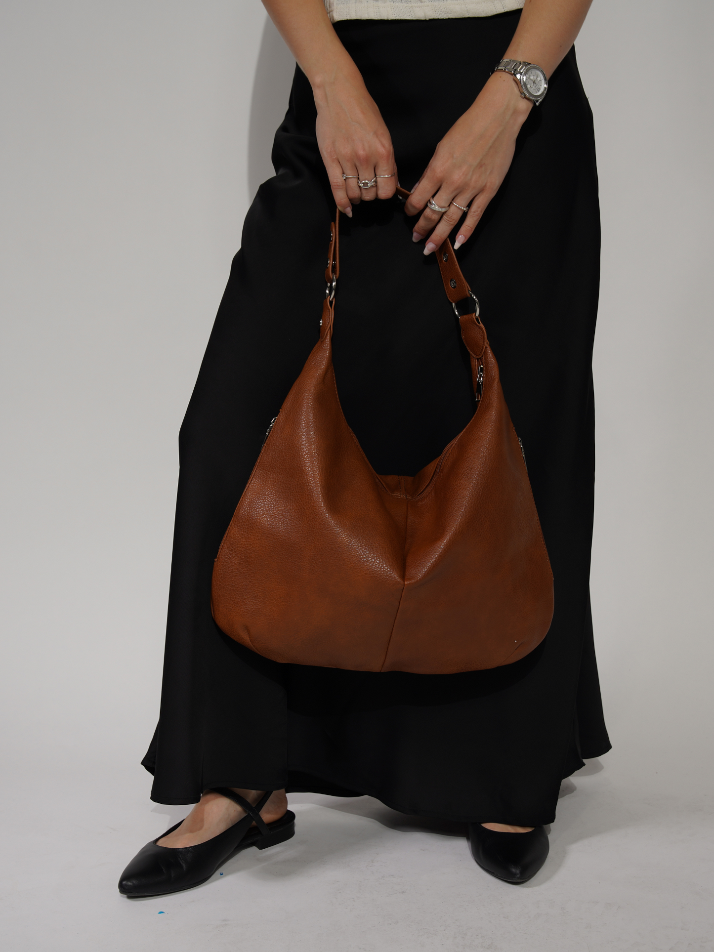 Kvinde med sort nederdel og brune lædersko holder en stor brun lædertaske. Mode, tilbehør, stilfuld håndtaske, elegant look.