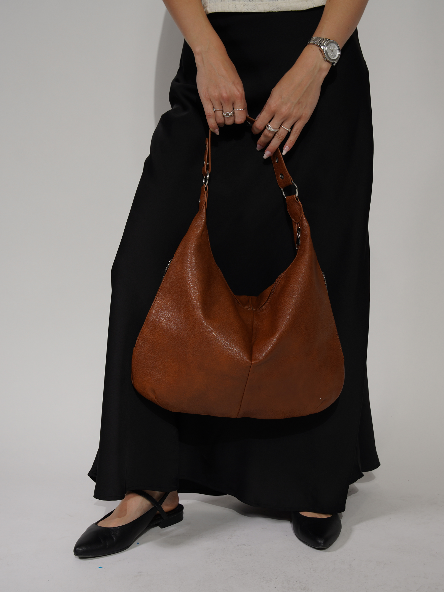 Kvinde med sort nederdel og brune lædersko holder en stor brun lædertaske. Mode, tilbehør, stilfuld håndtaske, elegant look.