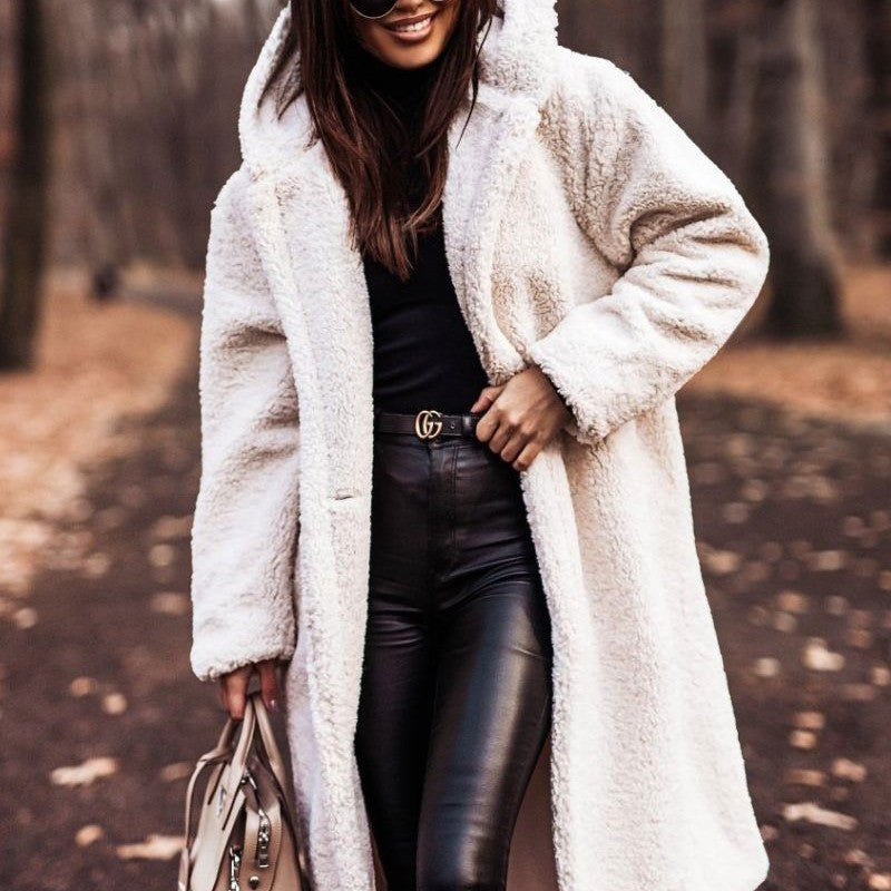 Femme portant un manteau en fausse fourrure blanc, pantalon en cuir noir, lunettes de soleil, tenant un sac à main beige, dans un parc automnal.