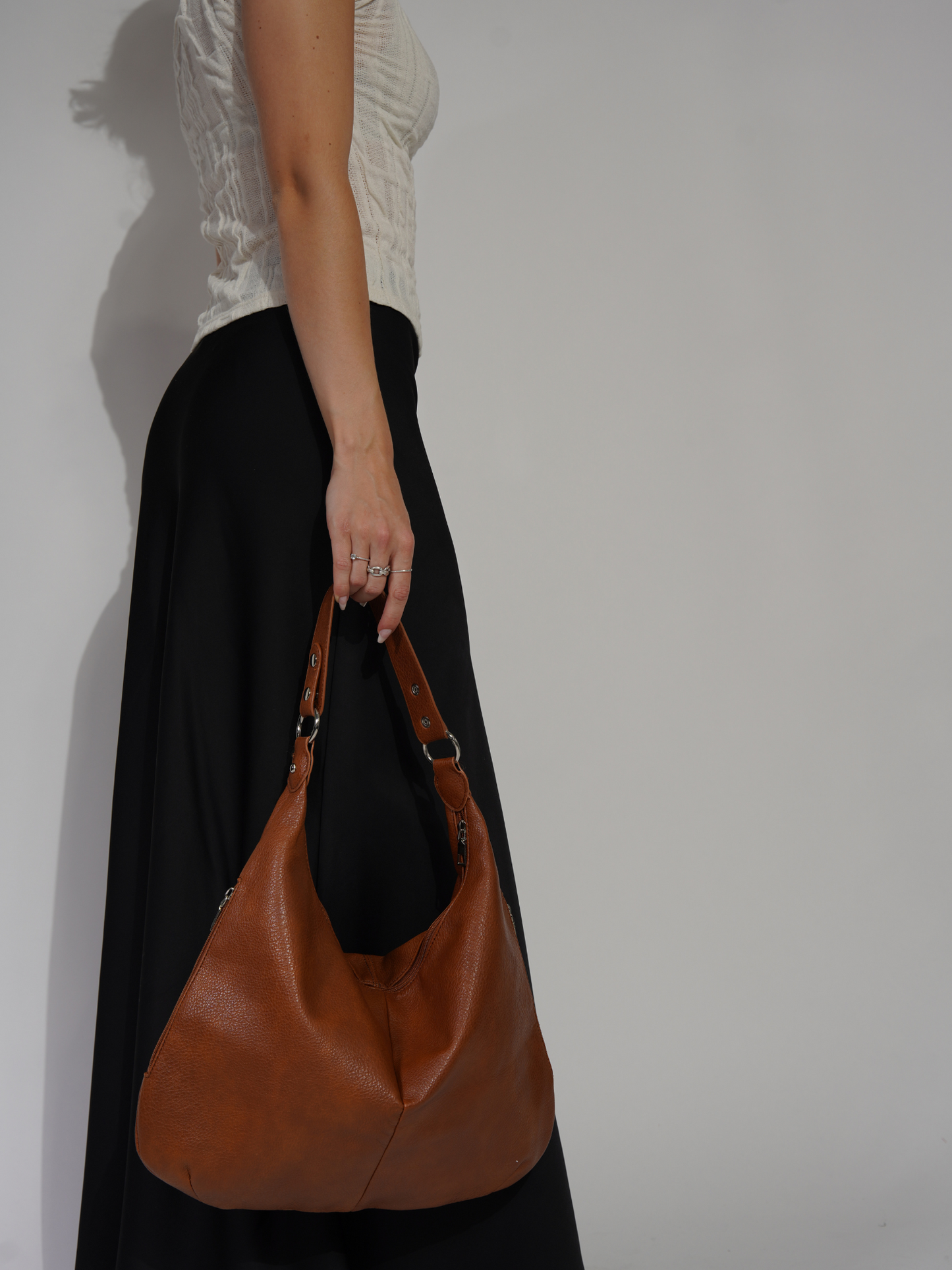 Kvinde med brun læderhåndtaske, iført sort nederdel og hvid top. Mode, stilfuld taske, moderne tilbehør, elegant look.