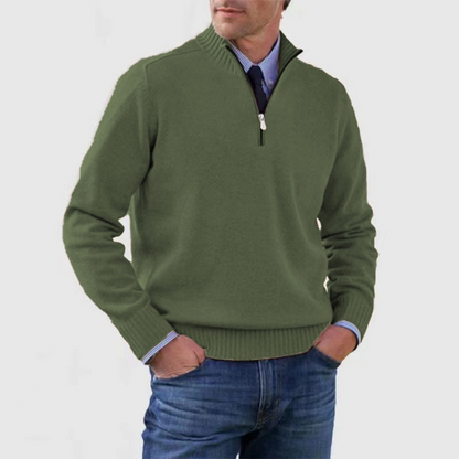 Homme portant un pull vert à col zippé, manches longues, sur une chemise bleue, avec un jean. Mode masculine élégante et décontractée.