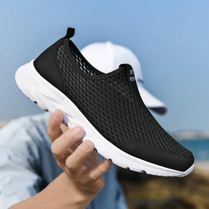 Chaussure de sport noire en maille respirante, semelle blanche, tenue par une main. Idéale pour la course et les activités extérieures.