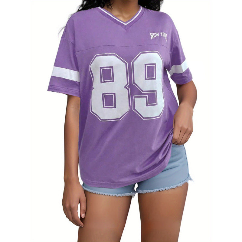 Femme portant un t-shirt violet avec le numéro 89 et "New York", associé à un short en jean. Mode décontractée, style urbain tendance.