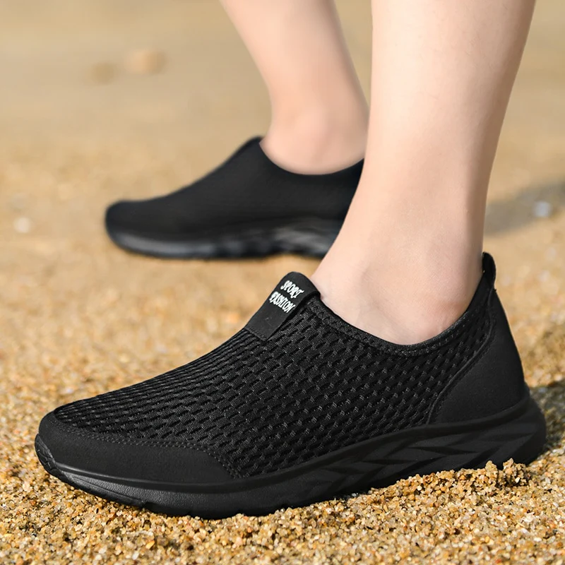 Chaussures de sport noires en maille respirante sur pieds, idéales pour la marche sur sable. Confortables, légères, parfaites pour activités extérieures.