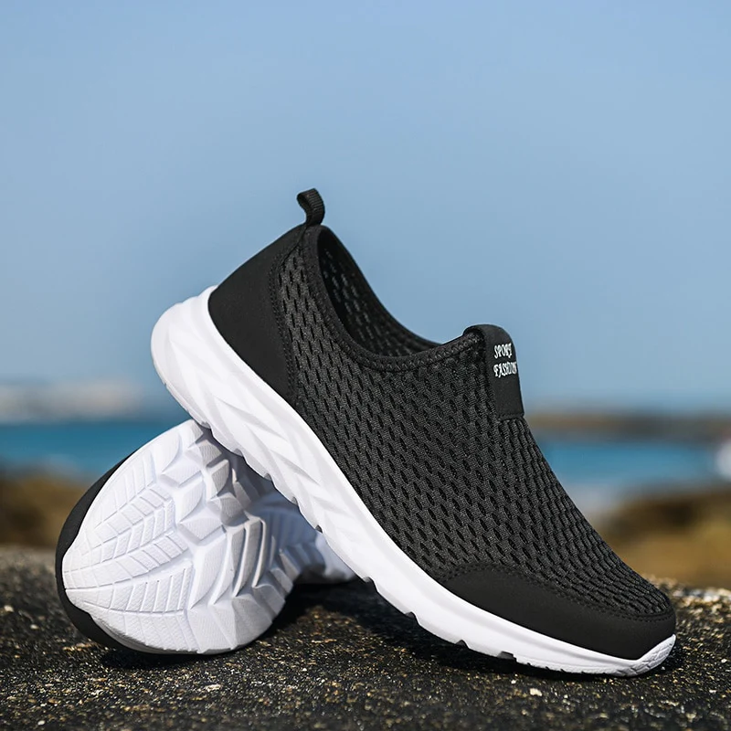 Chaussures de sport noires en maille respirante avec semelles blanches, posées sur un rocher en bord de mer, idéales pour la marche et le running.