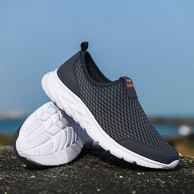 Chaussures de sport noires en maille respirante avec semelles blanches, posées sur un rocher en extérieur, idéales pour la course et le fitness.