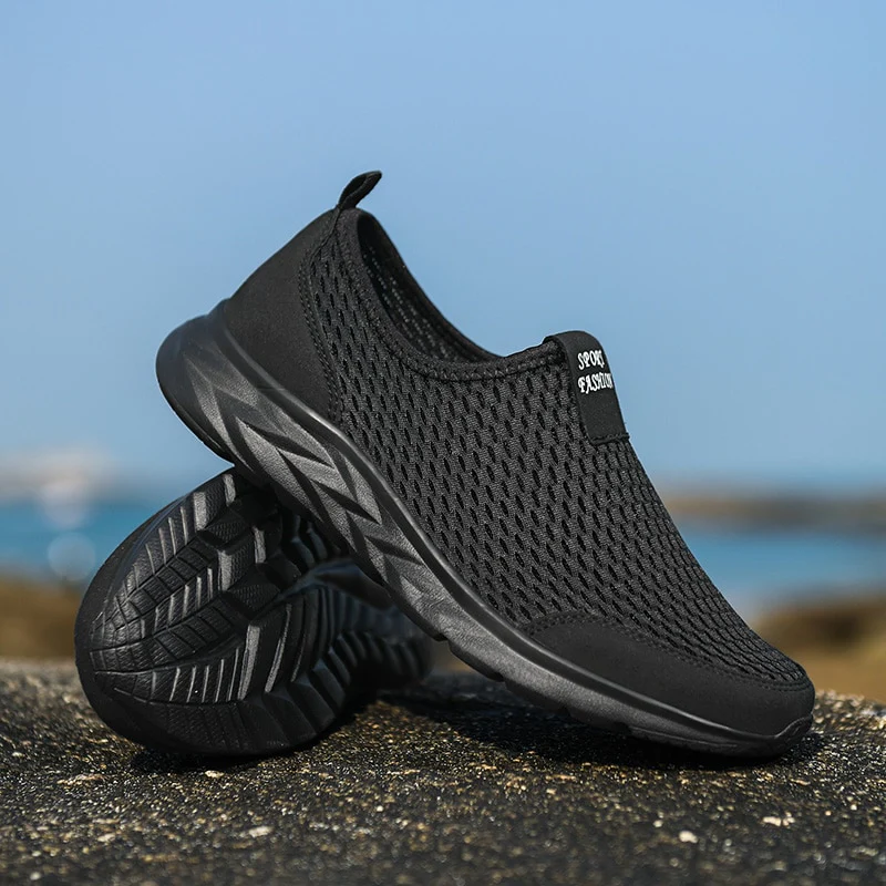 Chaussures de sport noires respirantes pour hommes sur fond de plage, semelle antidérapante, design moderne, idéales pour la course et le fitness.