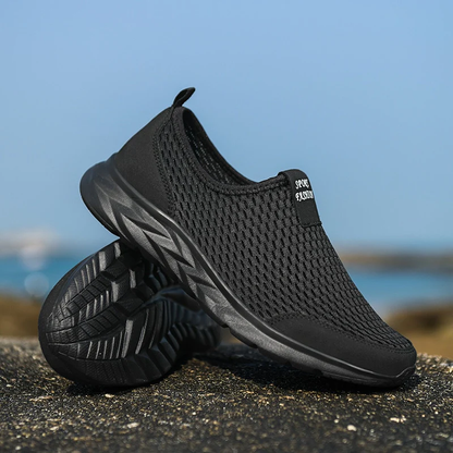 Chaussures de sport noires respirantes pour hommes sur fond de plage, semelle antidérapante, design moderne, idéales pour la course et le fitness.