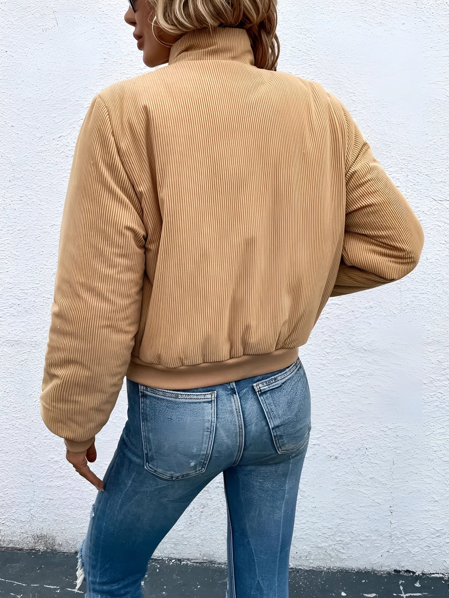 Tan corduroy bomber jacket for women, perfect for trendy fall outerwear, featuring a comfortable textile with a classic bomber style including full sleeves and a waist-length design, worn by a person standing, paired with jeans and a dress shirt.