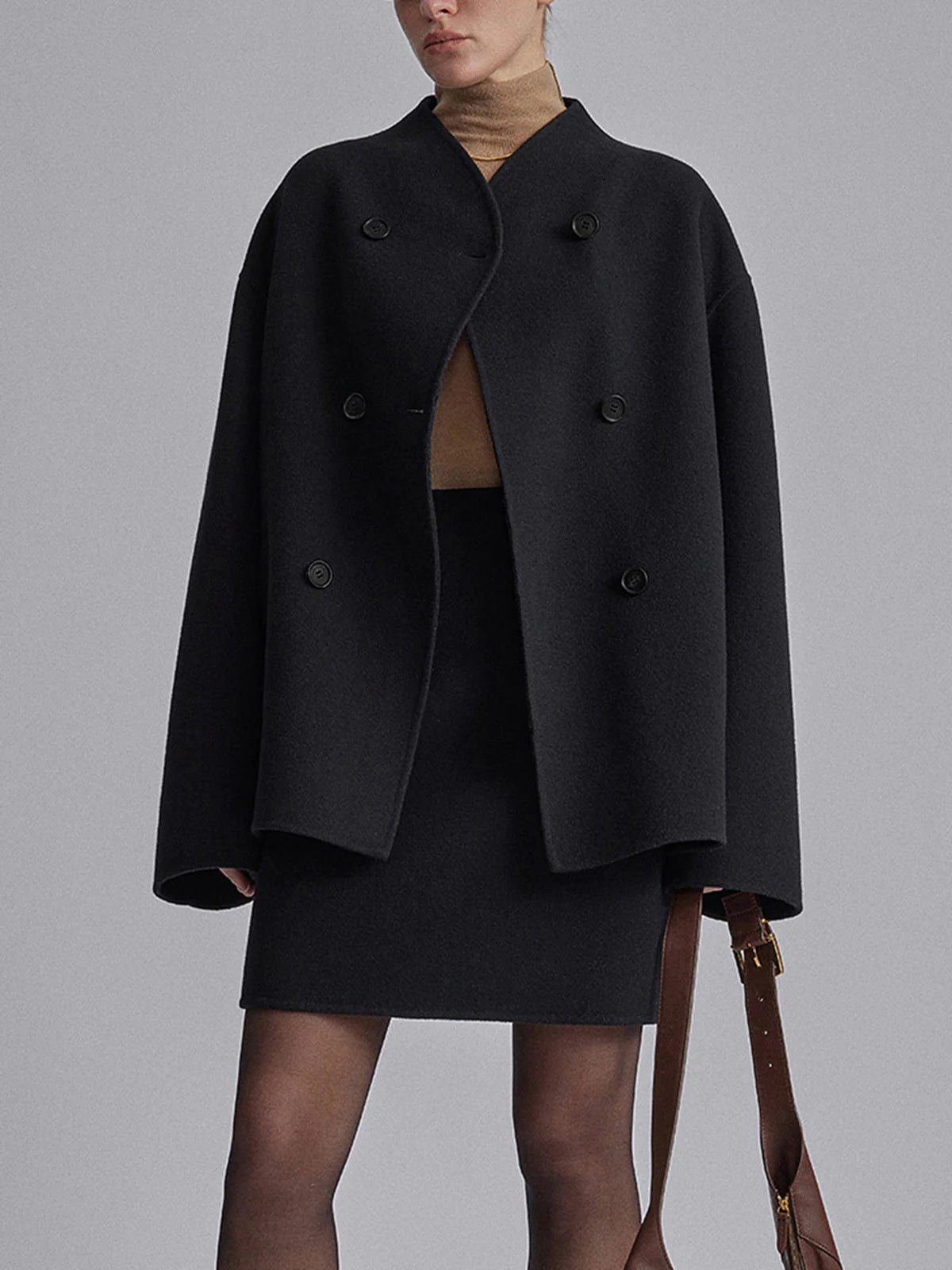 Femme portant un manteau noir oversize à double boutonnage, jupe assortie, col roulé beige, style élégant et moderne, mode automne-hiver.