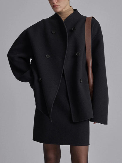 Femme portant un manteau noir oversize à double boutonnage, robe noire, col roulé beige, sac en cuir marron. Mode élégante et moderne.