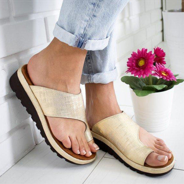Sandali donna beige con suola nera, indossati con jeans chiari. Design casual, comodi per l'estate. Fiore rosa in vaso bianco sullo sfondo.