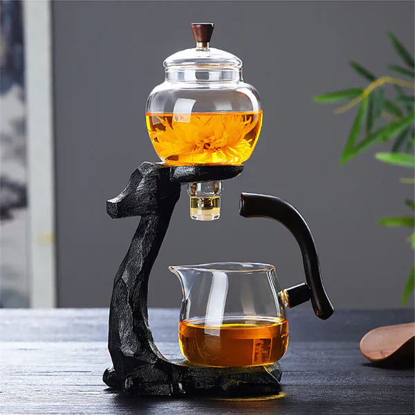 Glas-Teekanne mit schwarzem Holzgriff, Blumentee, modernes Design, auf Tisch, Hintergrundpflanze.
